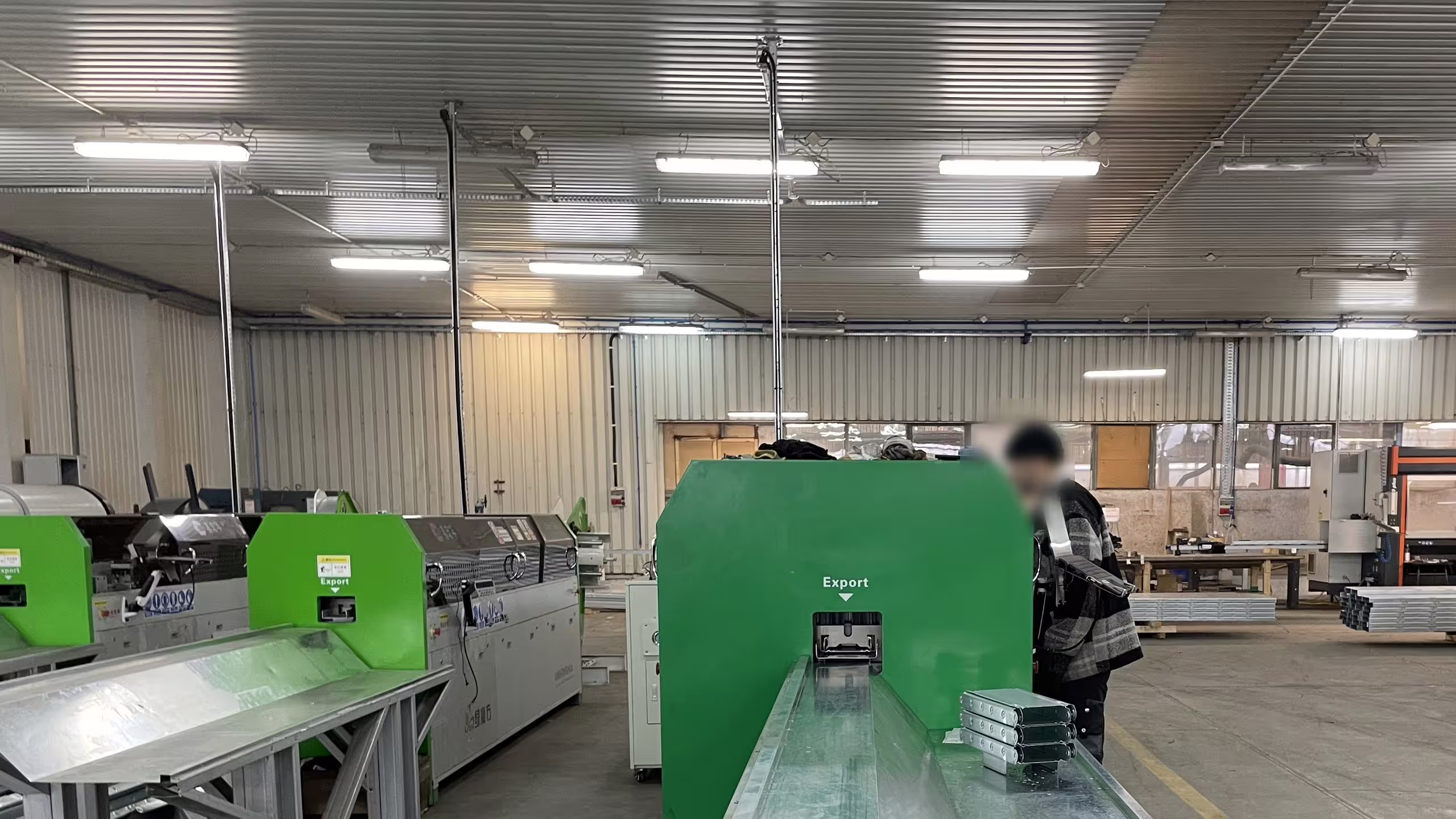 A galvanised section running out of the roll-forming line at Słupy, the operator working at the machine head and further profiling machines ranged down the bay
