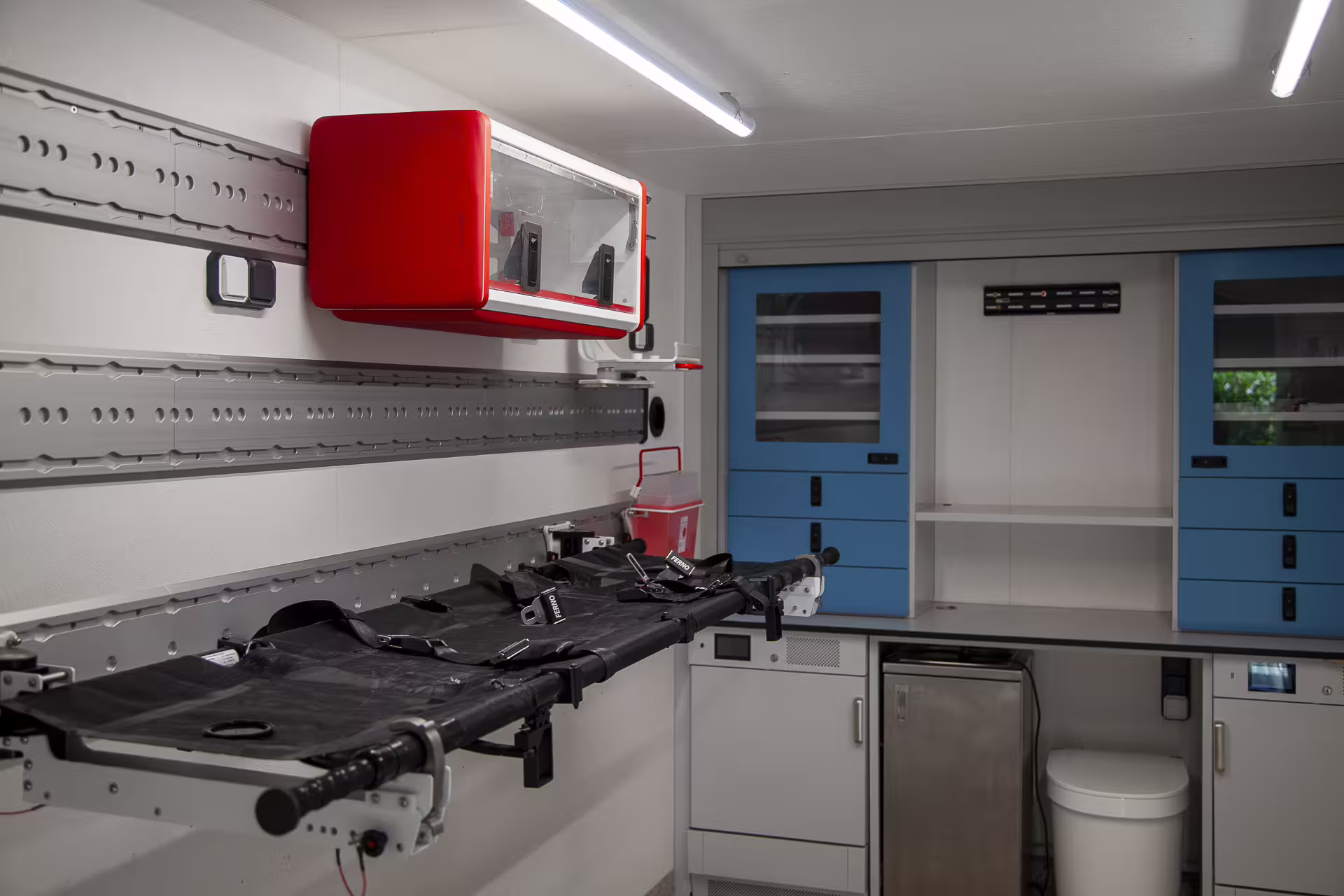 FlexiPod medical module with FERNO stretcher, wall-mounted kit box, rail system and blue equipment cabinets.
