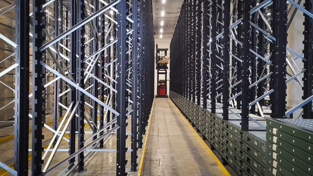 Looking down a narrow aisle between two runs of tall IARS racking loaded with boxed stock, the bays rising the full height of the building and rail lines set into the aisle floor