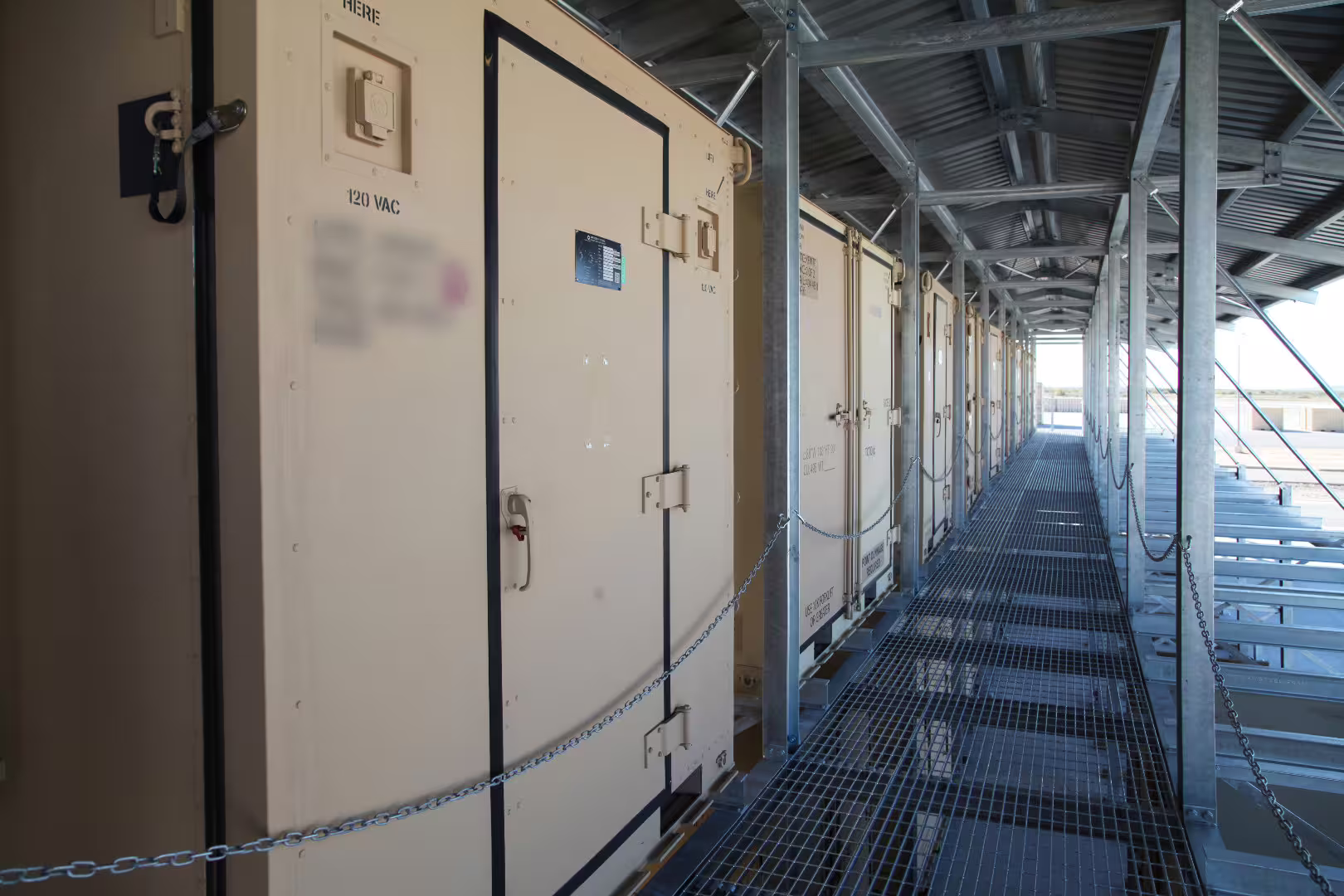 Covered walkway along a row of tan military containers on the upper tier of a two-storey container racking structure