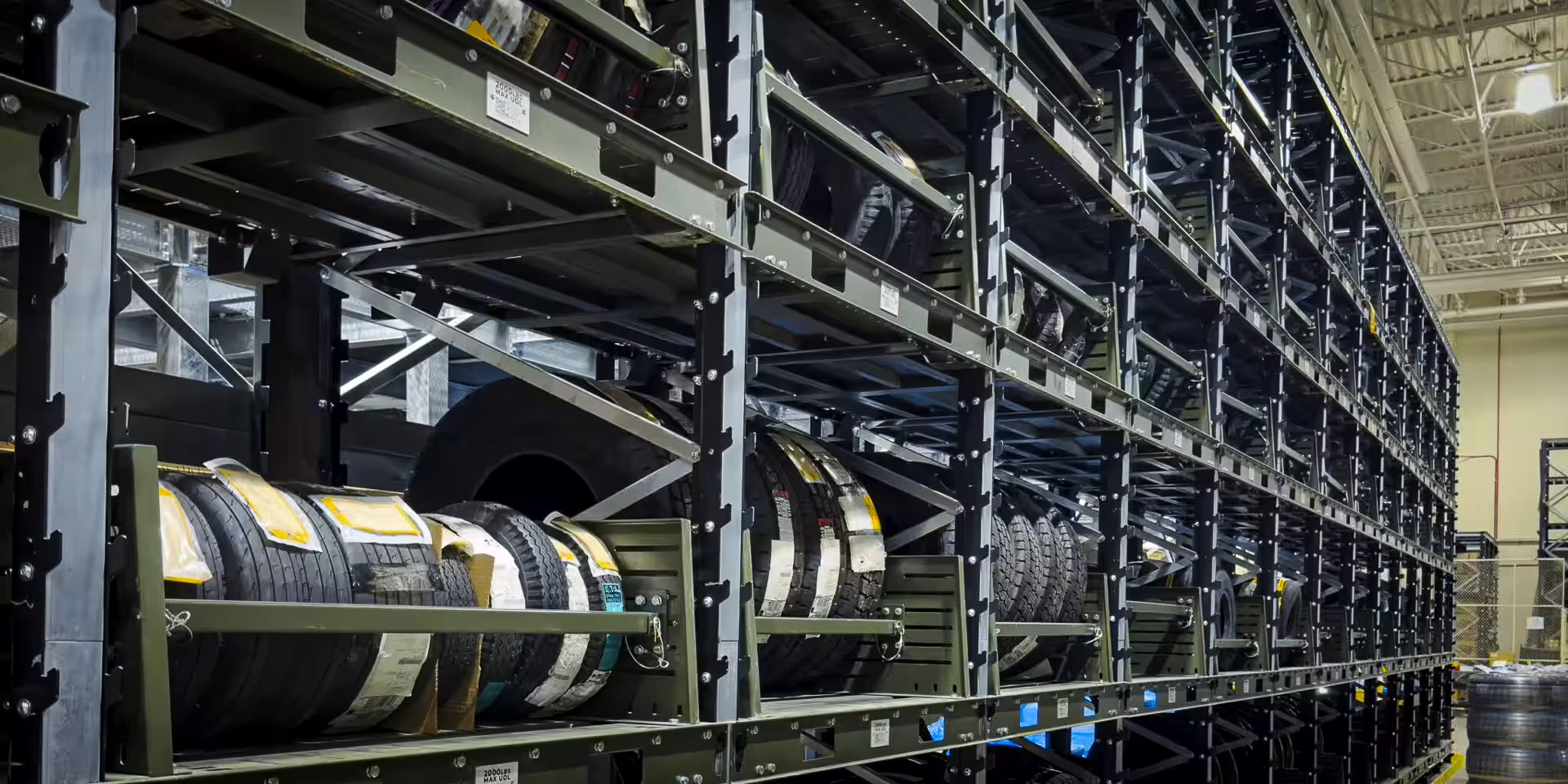 Long runs of green IARS racking filled with stacked vehicle tyres, each beam carrying a small white rated-capacity plate reading 2000LBS MAX UDL