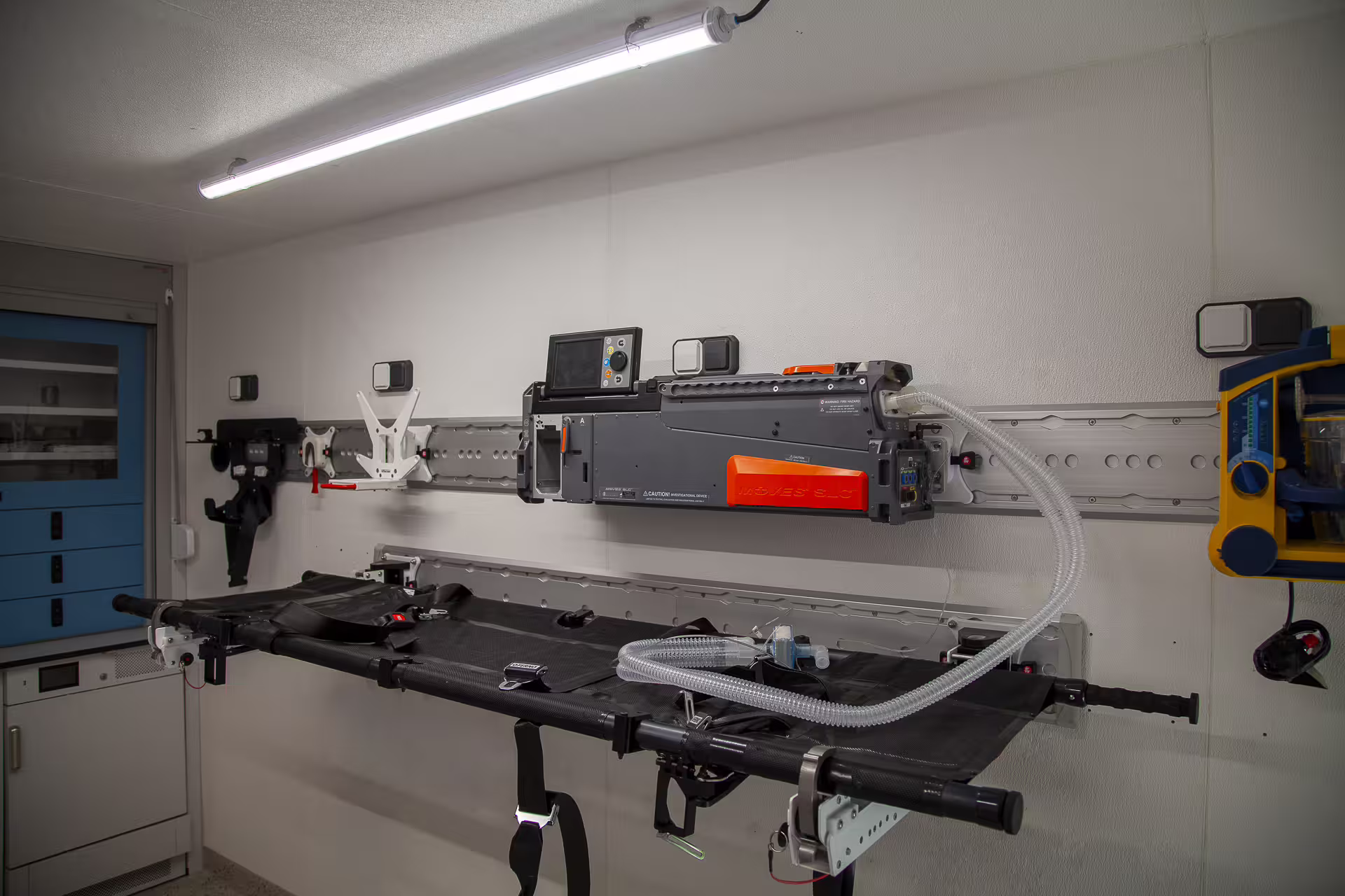 FlexiPod medical module interior with stretcher, rail-mounted MOVES SLC life-support unit and defibrillator.