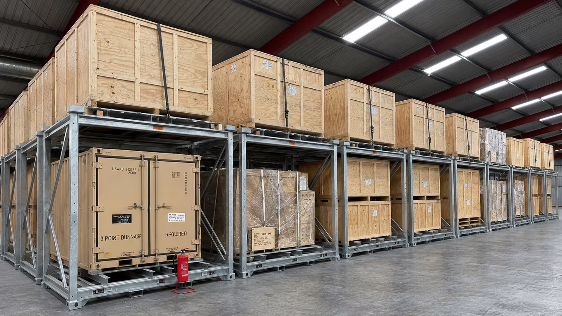 A long row of galvanised CargoCuber frames receding down a warehouse, each carrying timber crates and palletised loads on two levels