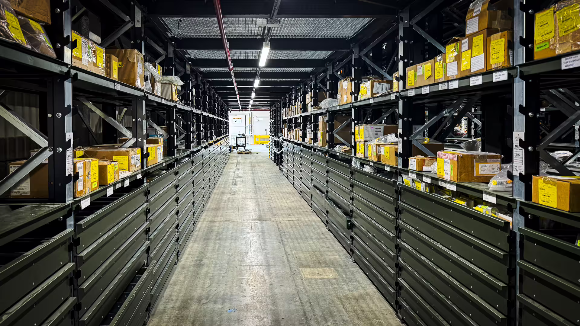 A long warehouse aisle running to a vanishing point, both sides filled from floor to waist height with rank after rank of closed green RackMezz drawer units