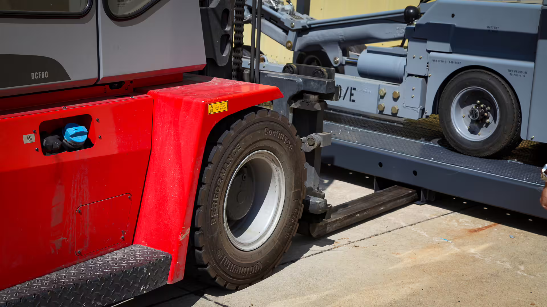 A red heavy-duty forklift with its forks under a loaded RollingStack crate, the crate's deck and a wheeled plant unit visible above the tines