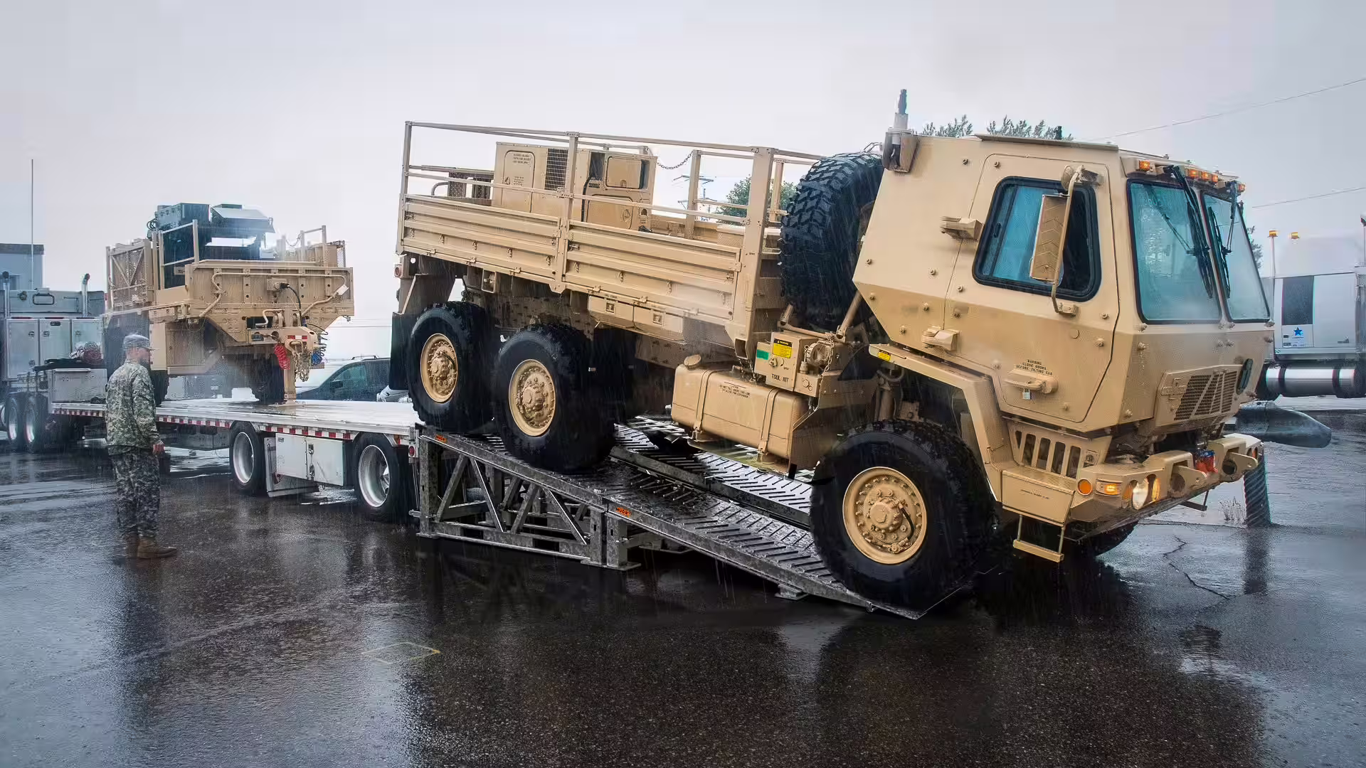Military cargo truck driving off a flatbed trailer down MUDR-PD50 ramp tracks in the rain