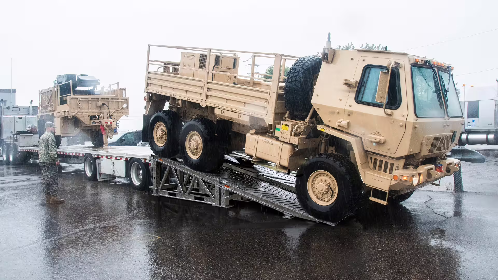 Military cargo truck driving off a flatbed trailer down MUDR-PD50 ramp tracks in the rain