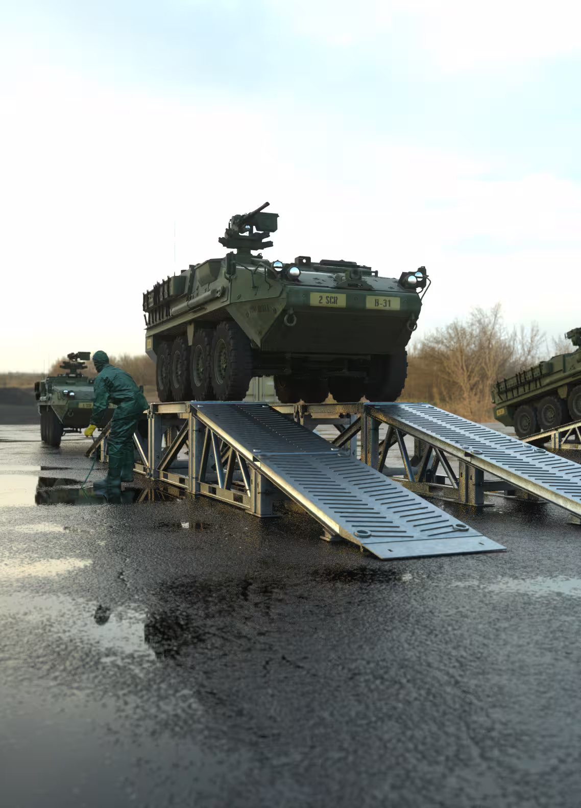 Operator in protective suit washing a Stryker from below on a MUDR-PD/WR inspection ramp