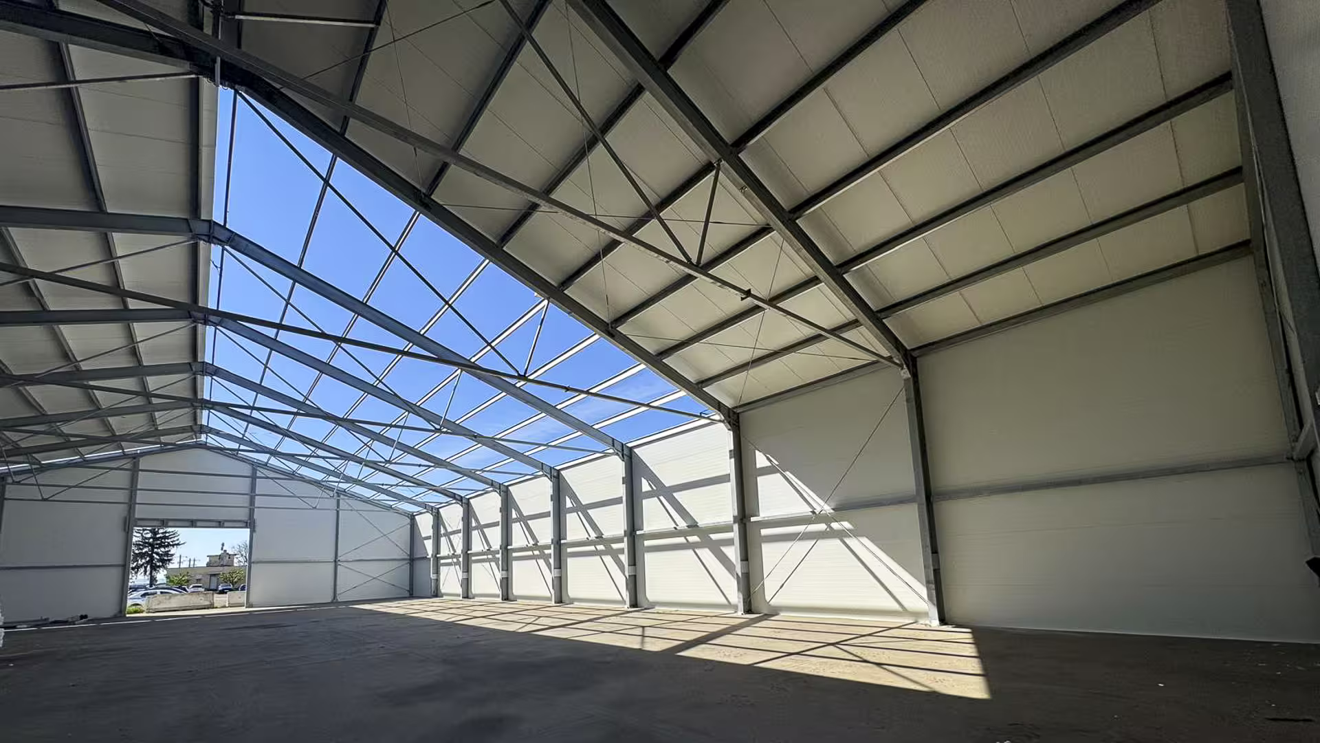 Interior of a DMTSS building under construction: galvanised steel portal frames and insulated panel walls, with part of the roof still open to the sky and a large doorway in the far end wall