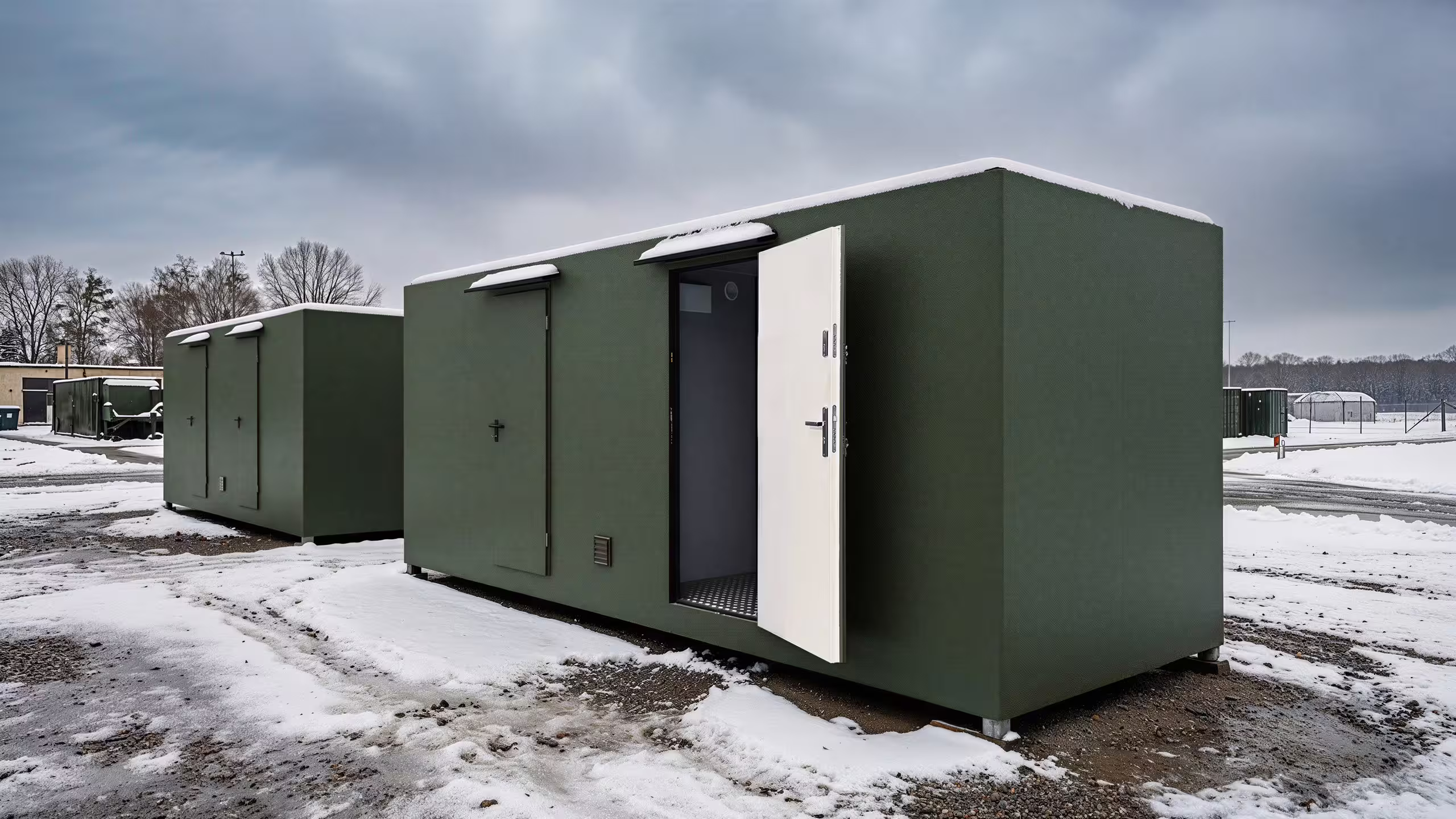 Visualisation of a BunkBox unit on frozen ground with its entrance door swung open, the chequerplate threshold and interior visible beyond, a second unit in line behind it under a heavy overcast sky