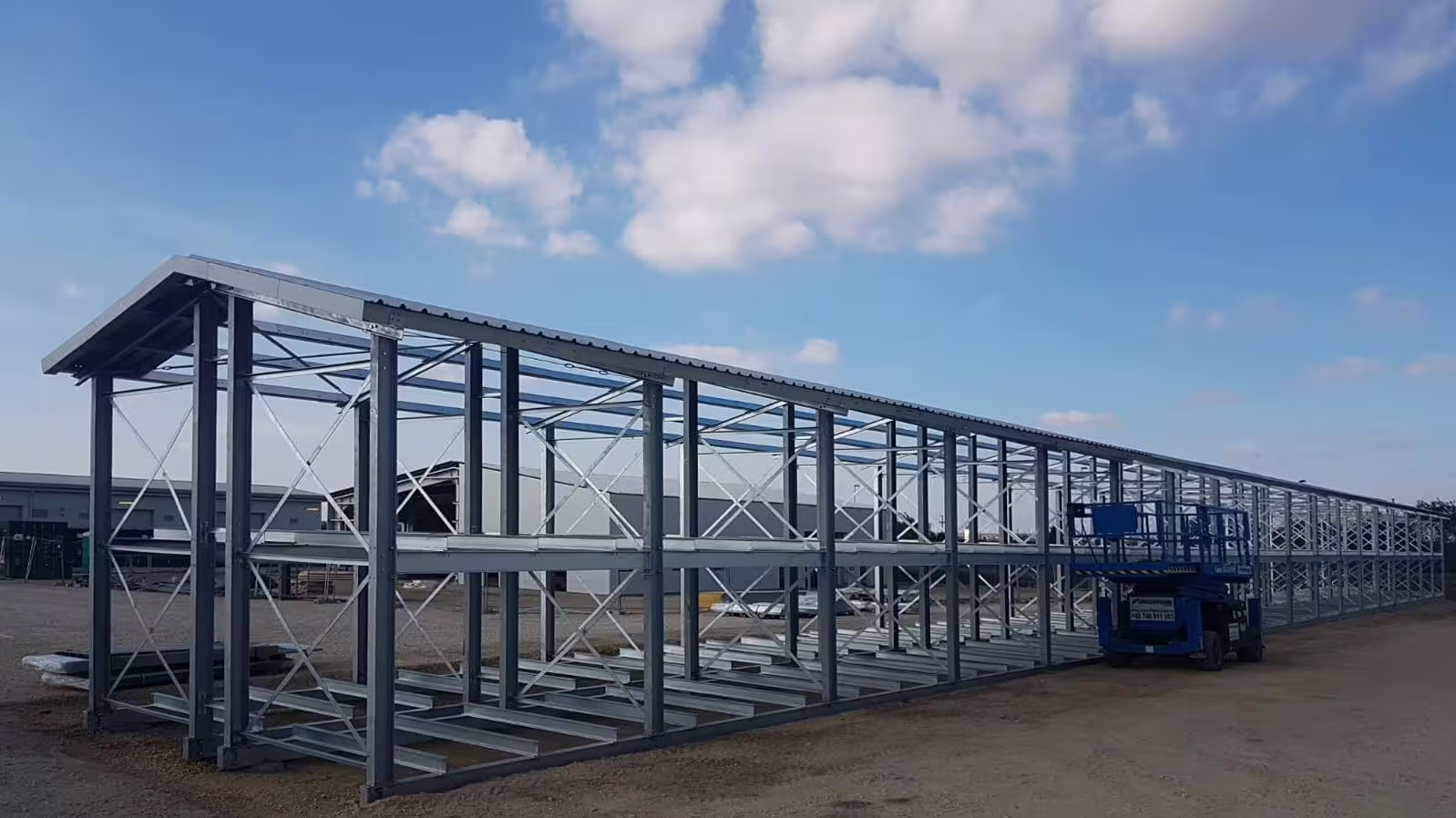 A long open Laydown CargoRack run standing empty on hardstanding under a blue sky, its low galvanised frames and roof stretching away