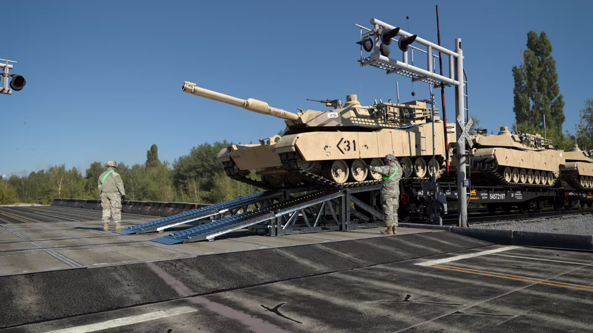 Abrams tanks offloading from railcars over a MUDR-PD90 ramp, soldiers marshalling