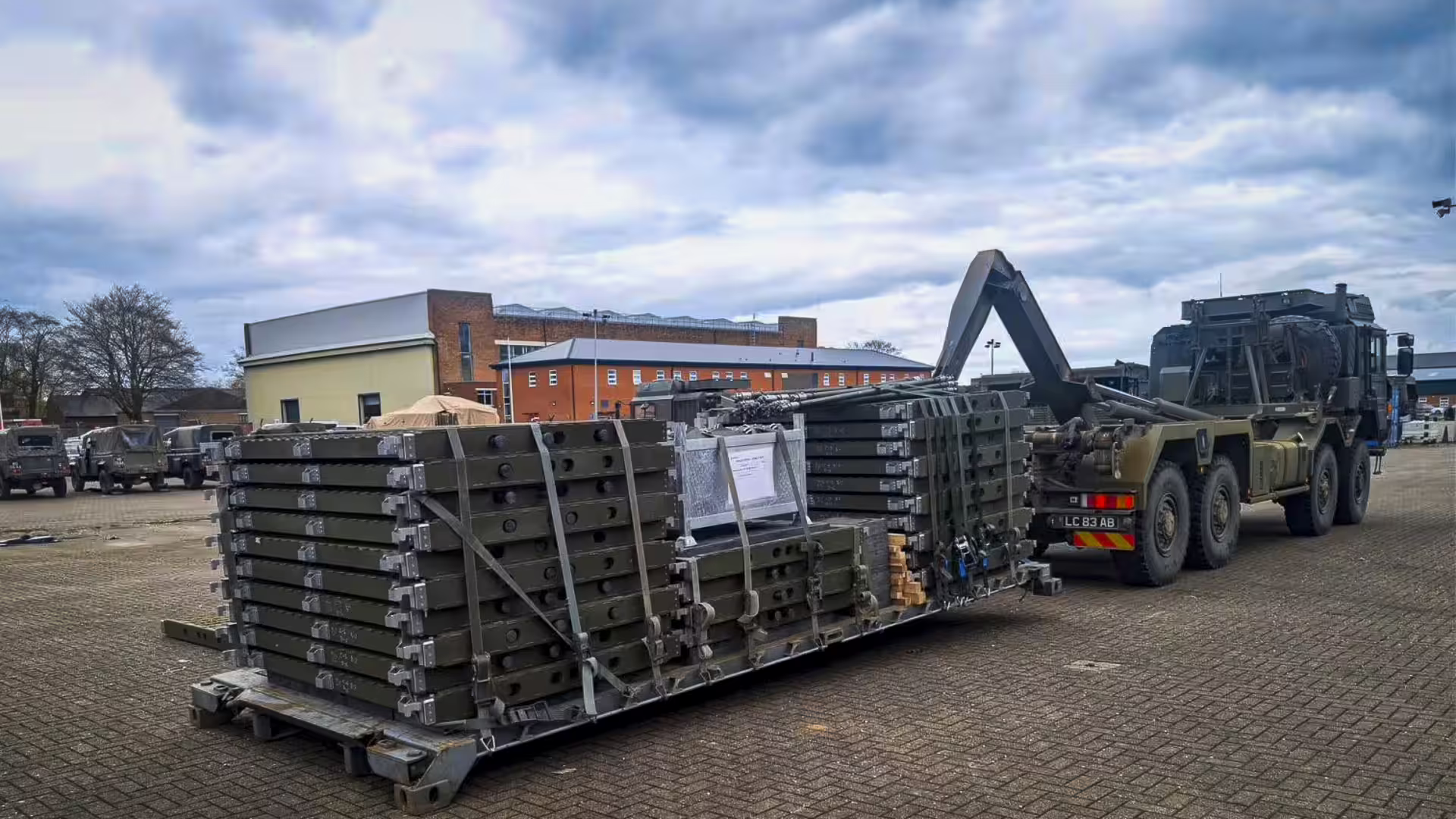 Packed RM90 mat sections strapped on a flatrack beside a military hook-loader truck
