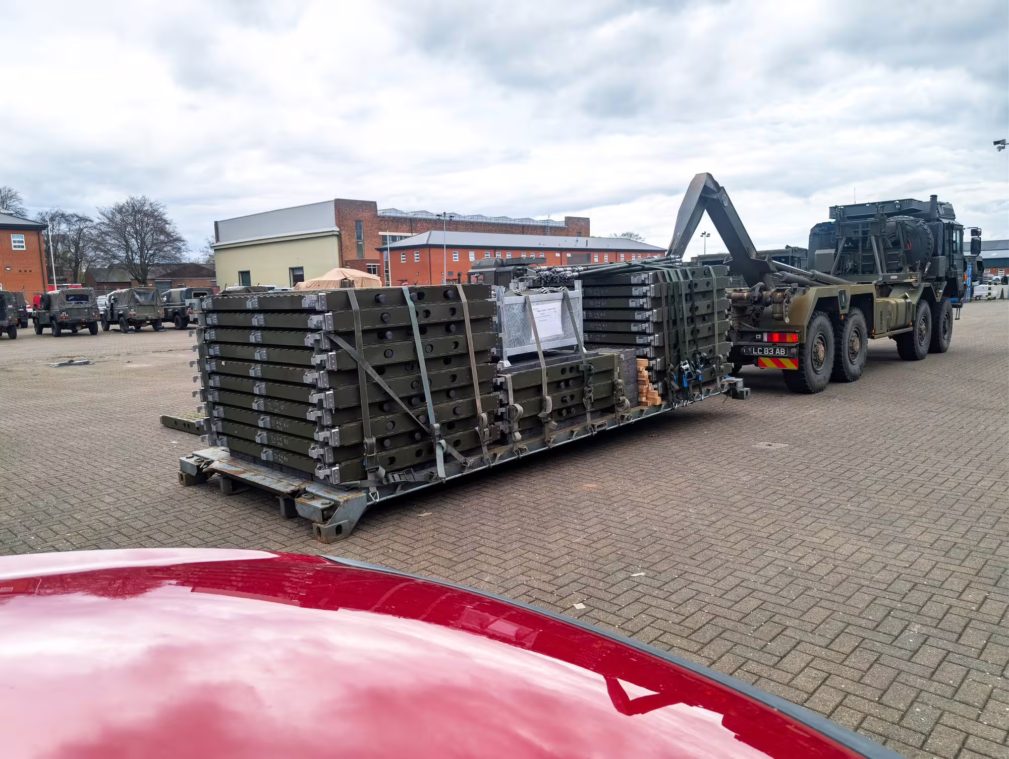 Packed RM90 mat sections strapped on a flatrack beside a military hook-loader truck