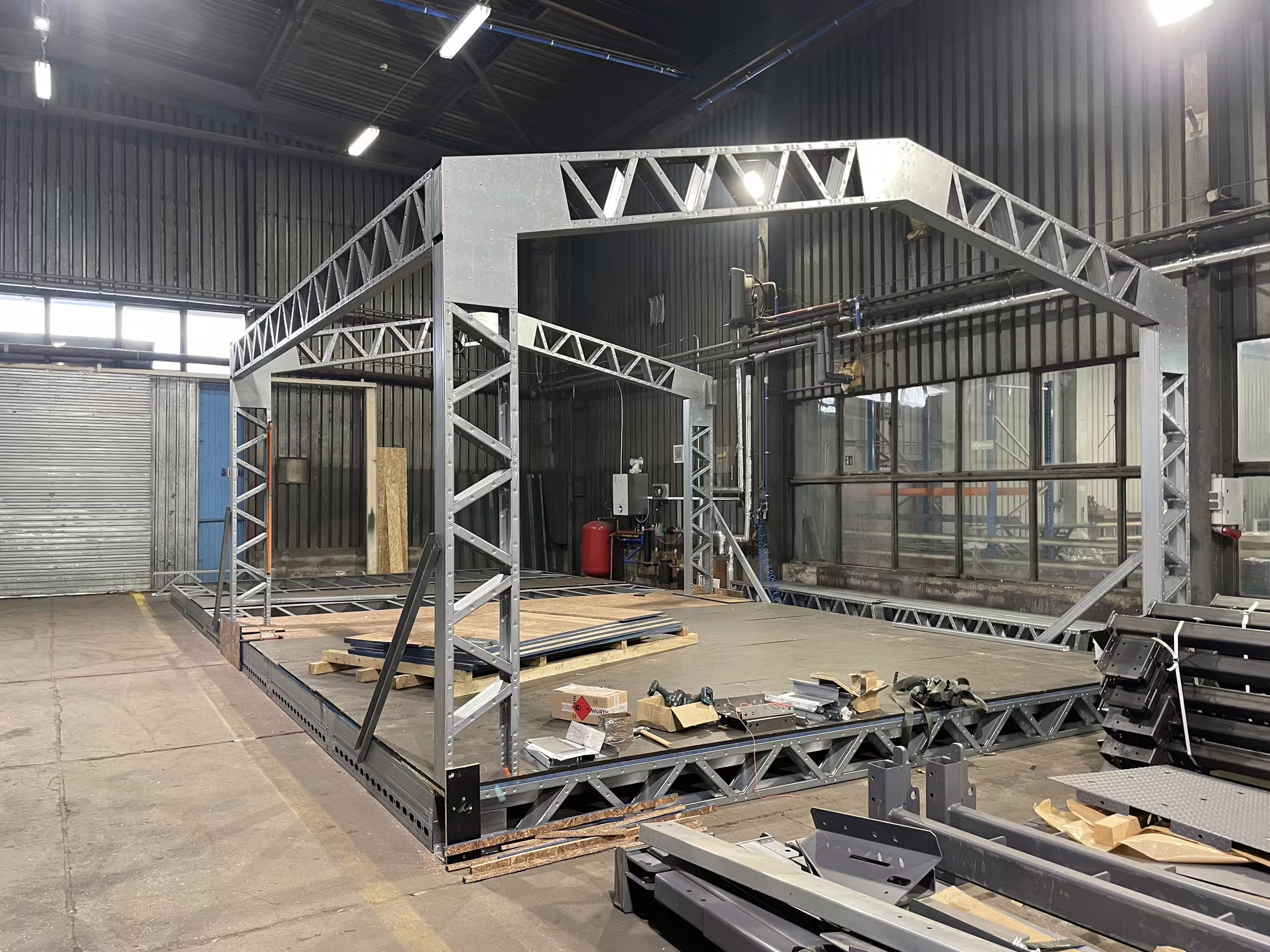A Tactical Shelter bay assembled inside BANAIR's Poland factory: lattice trusses and portal frames standing on the shop floor with panels and sections stacked behind