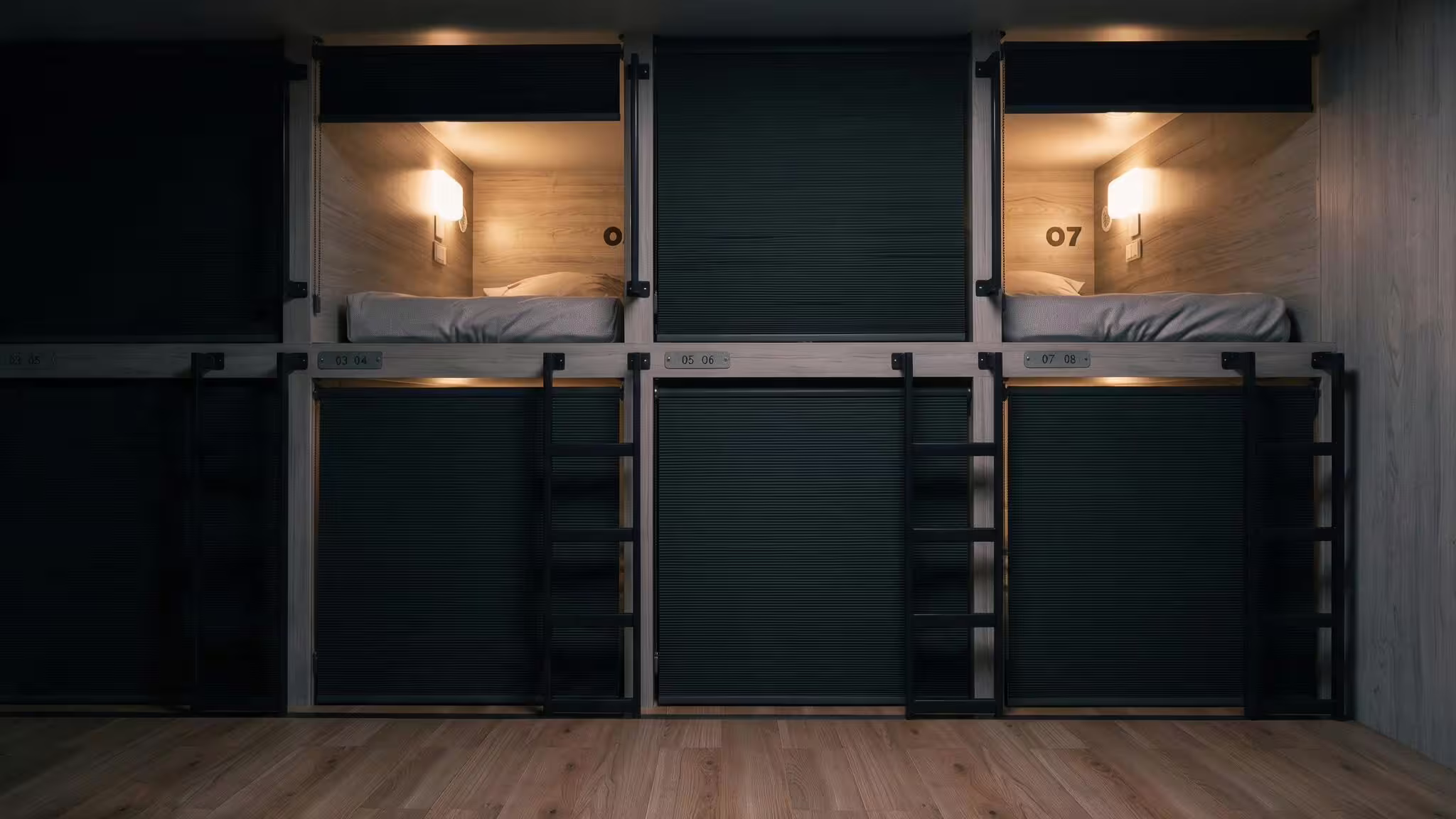 A run of enclosed bunk pods inside a BunkBox module with their privacy shutters drawn down, two pods left open and lit