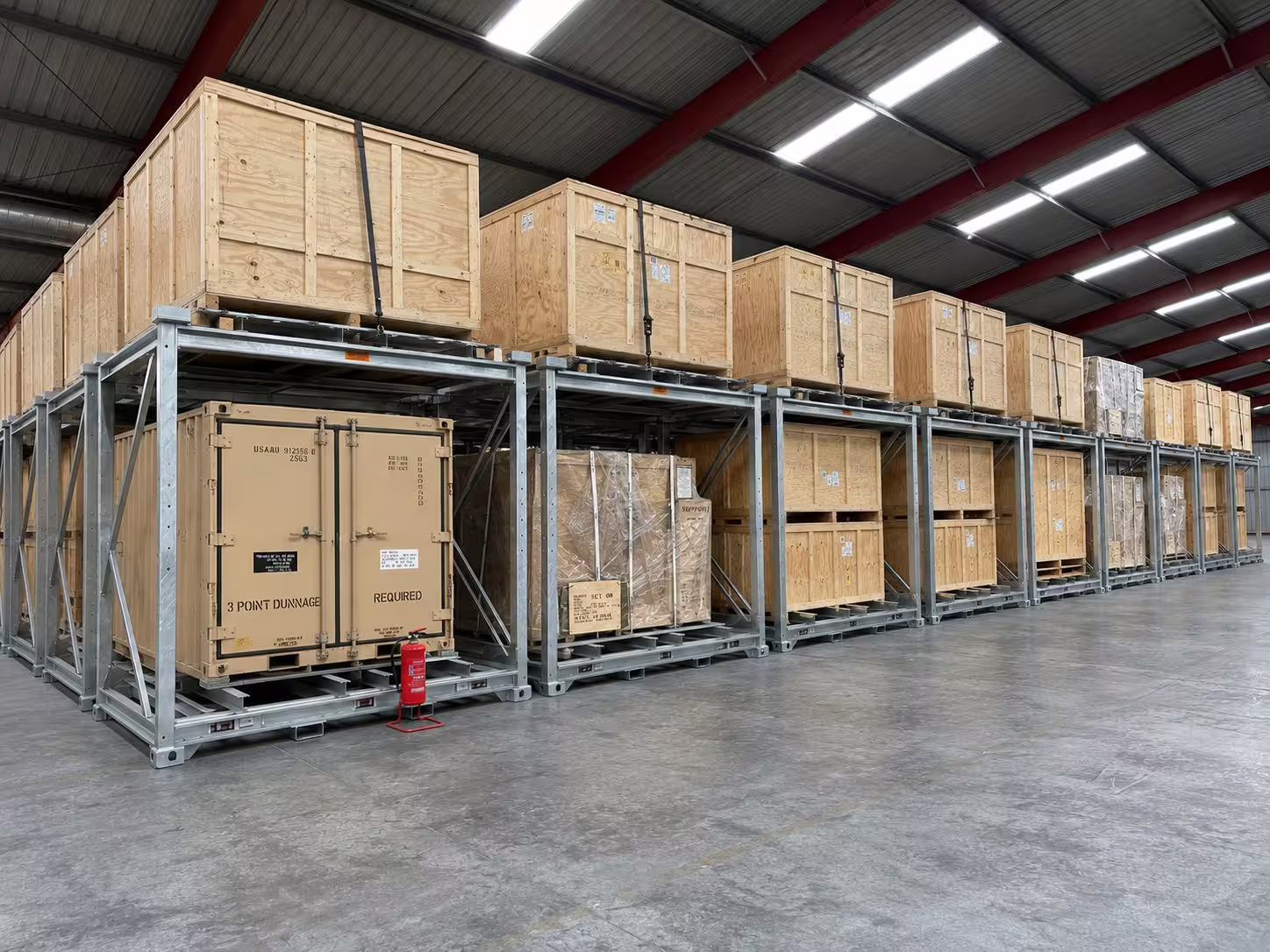 A long row of galvanised CargoCuber frames receding down a warehouse, each carrying timber crates and palletised loads on two levels