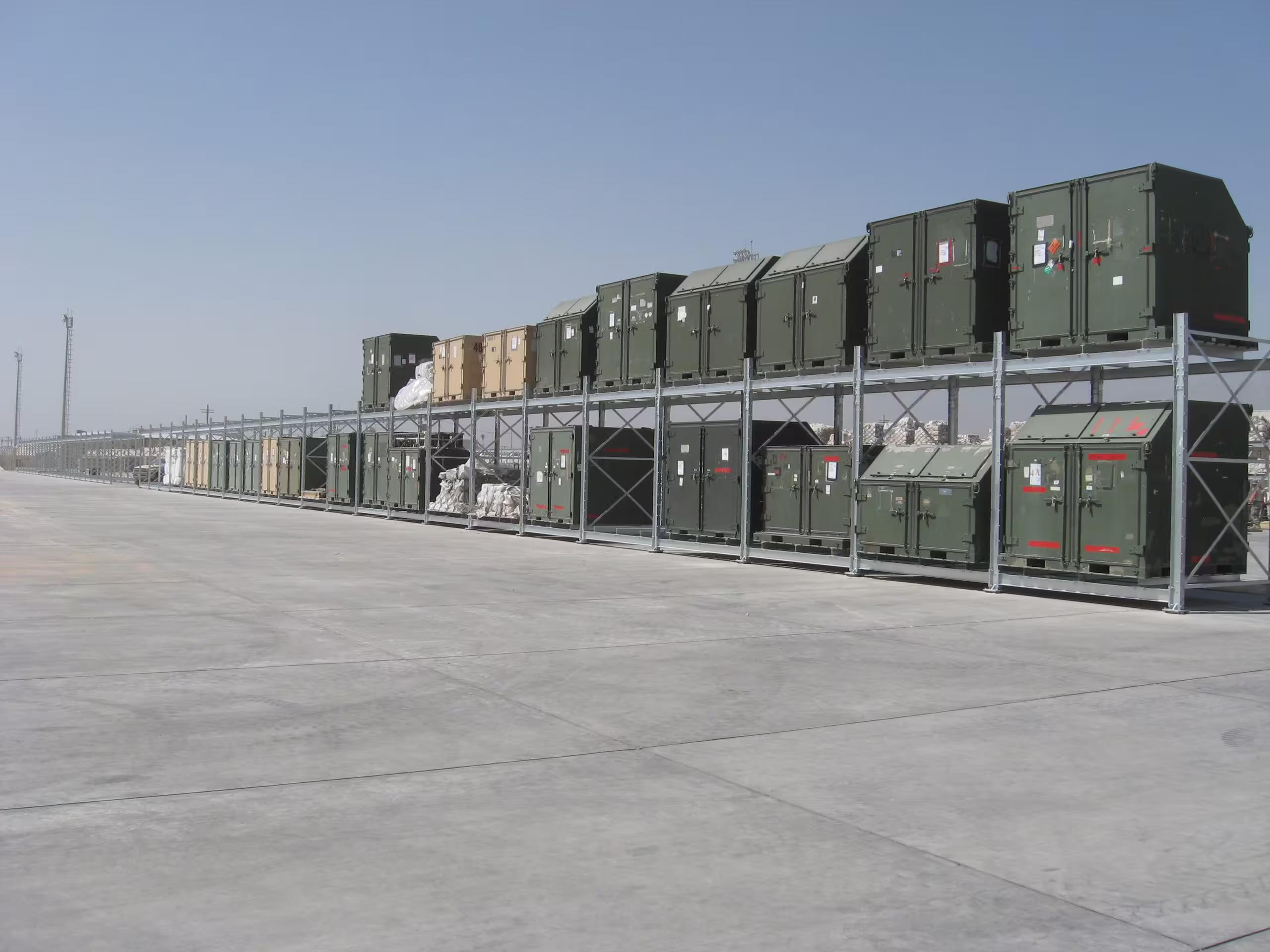 A long single-level CargoRack run on desert hardstanding, olive and tan containers and crated stores filling the bays along its length under a clear sky