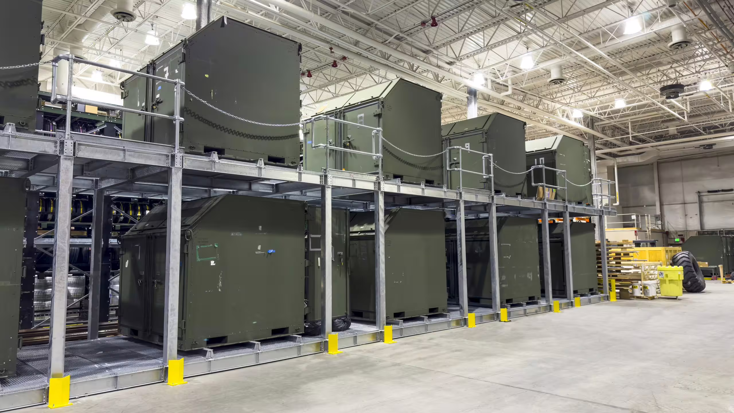 A two-level All Access CargoRack run inside a hangar, olive shelters and containers on both levels with open galvanised walkways and handrails between them