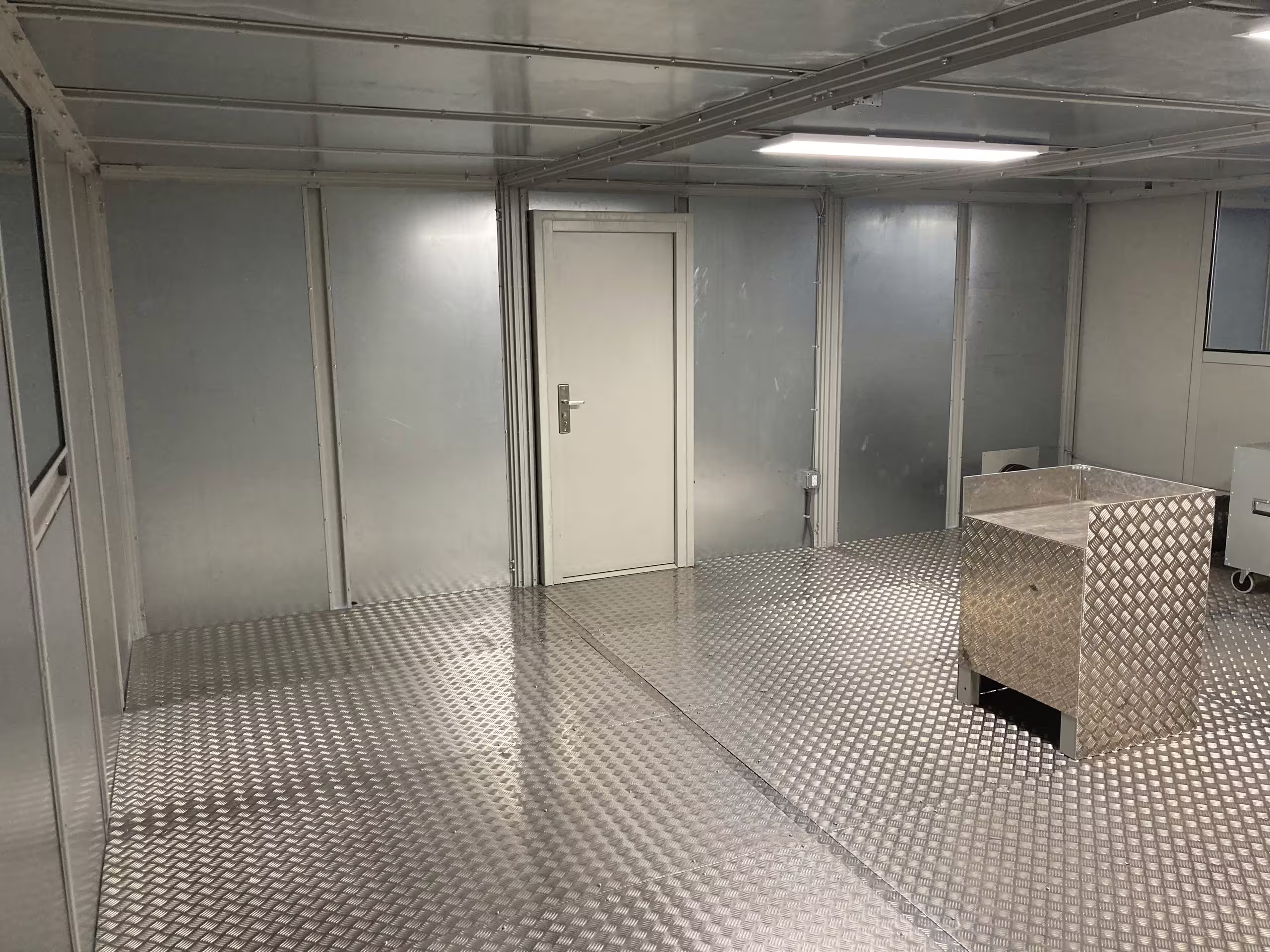 The chamber interior looking back toward the entry door, burner pedestal to one side, observation glazing along the partition and continuous ceiling lighting overhead