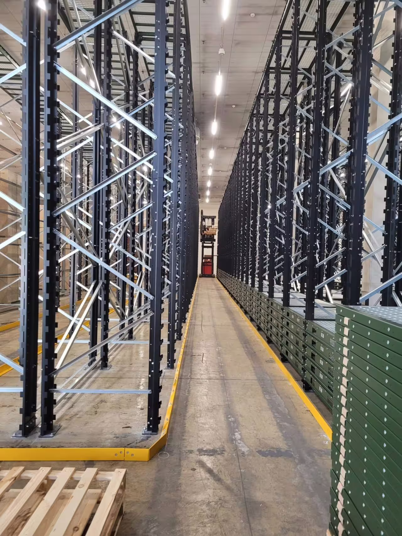 Looking down a narrow aisle between two runs of tall IARS racking loaded with boxed stock, the bays rising the full height of the building and rail lines set into the aisle floor
