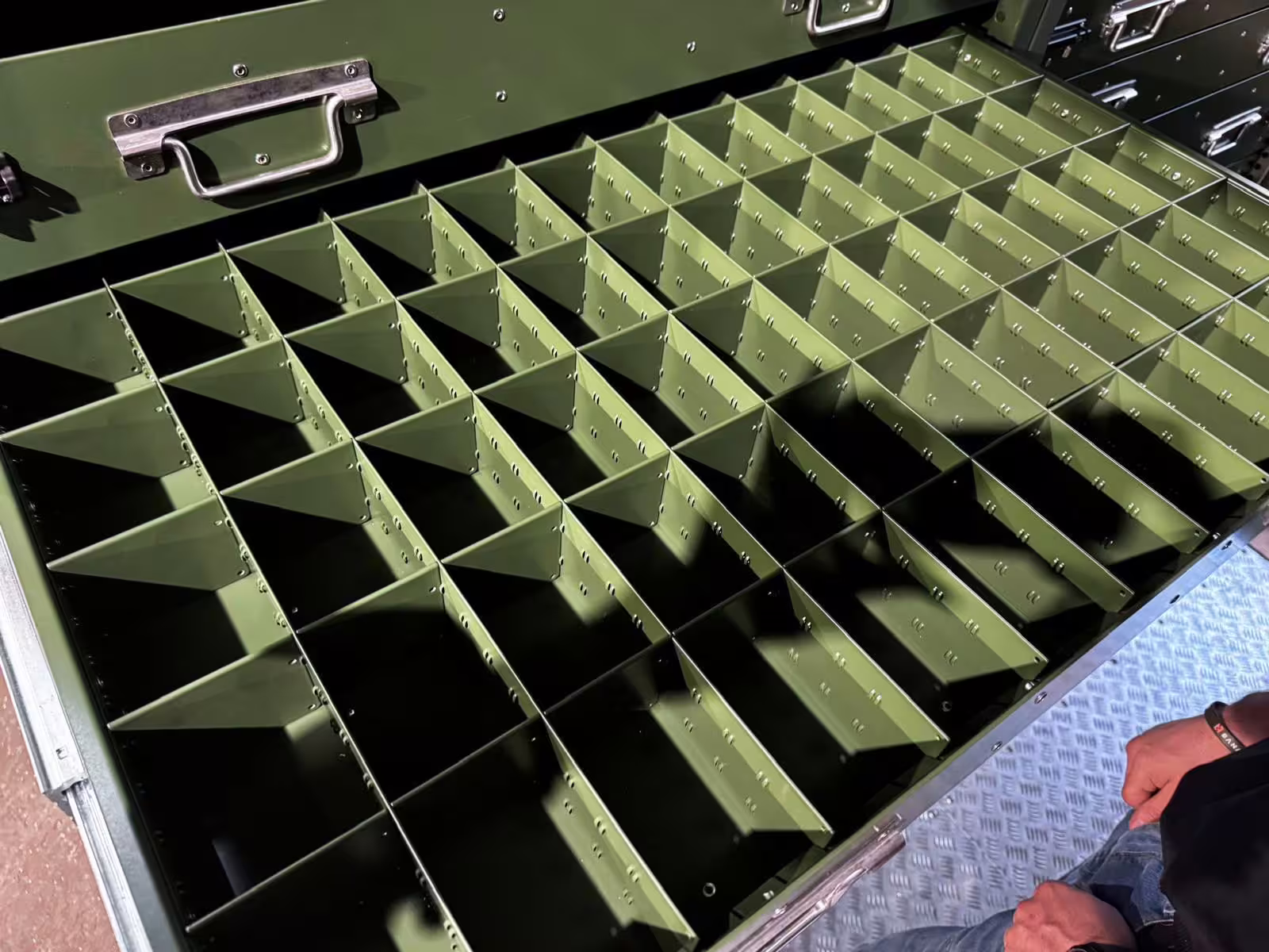 A close view of a green powder-coated steel divider grid inside a Rackbox drawer, the compartment walls slotted together over a chequer-plate base