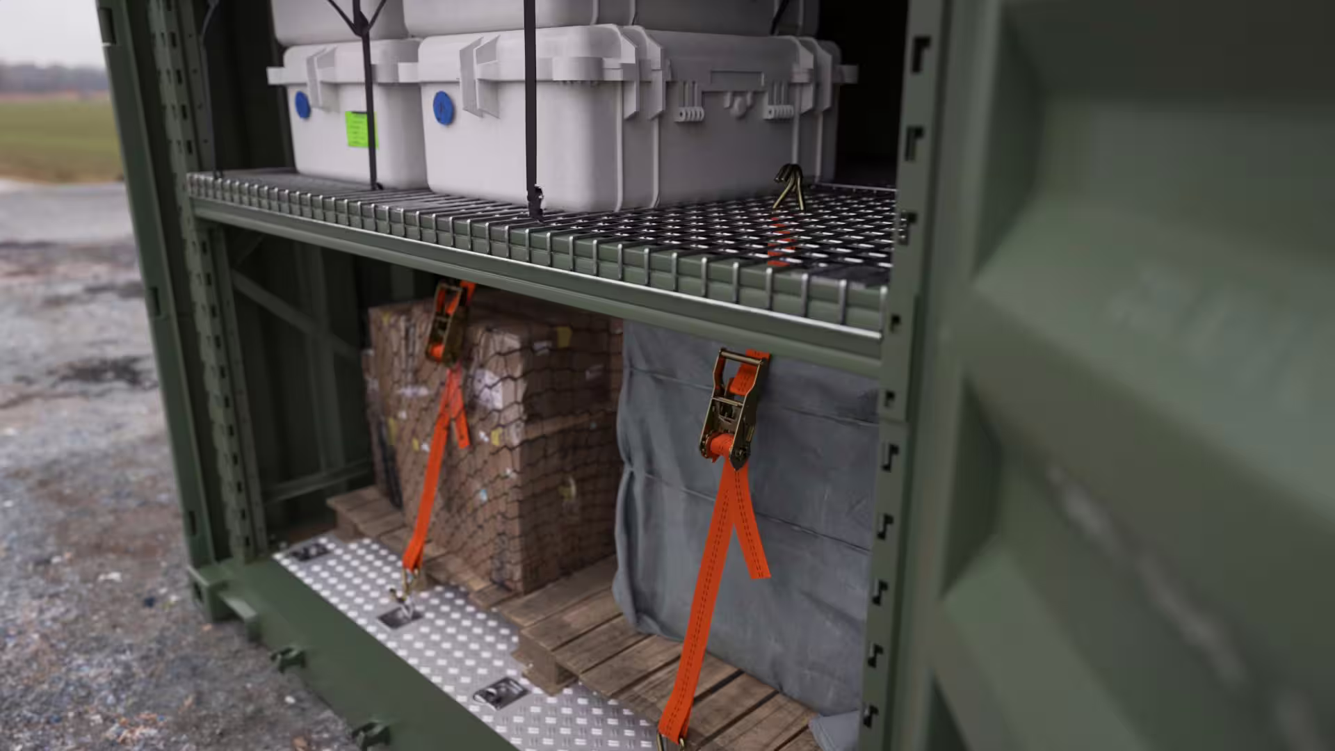 One module bay combining a wire-mesh deck shelf carrying white transit cases above with two palletised loads on the container floor below, held down by orange ratchet straps