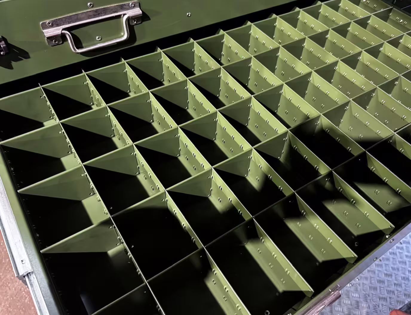 Looking down into an open module drawer subdivided by a grid of thin green dividers into rows of small compartments, with the drawer's stainless handle at the top