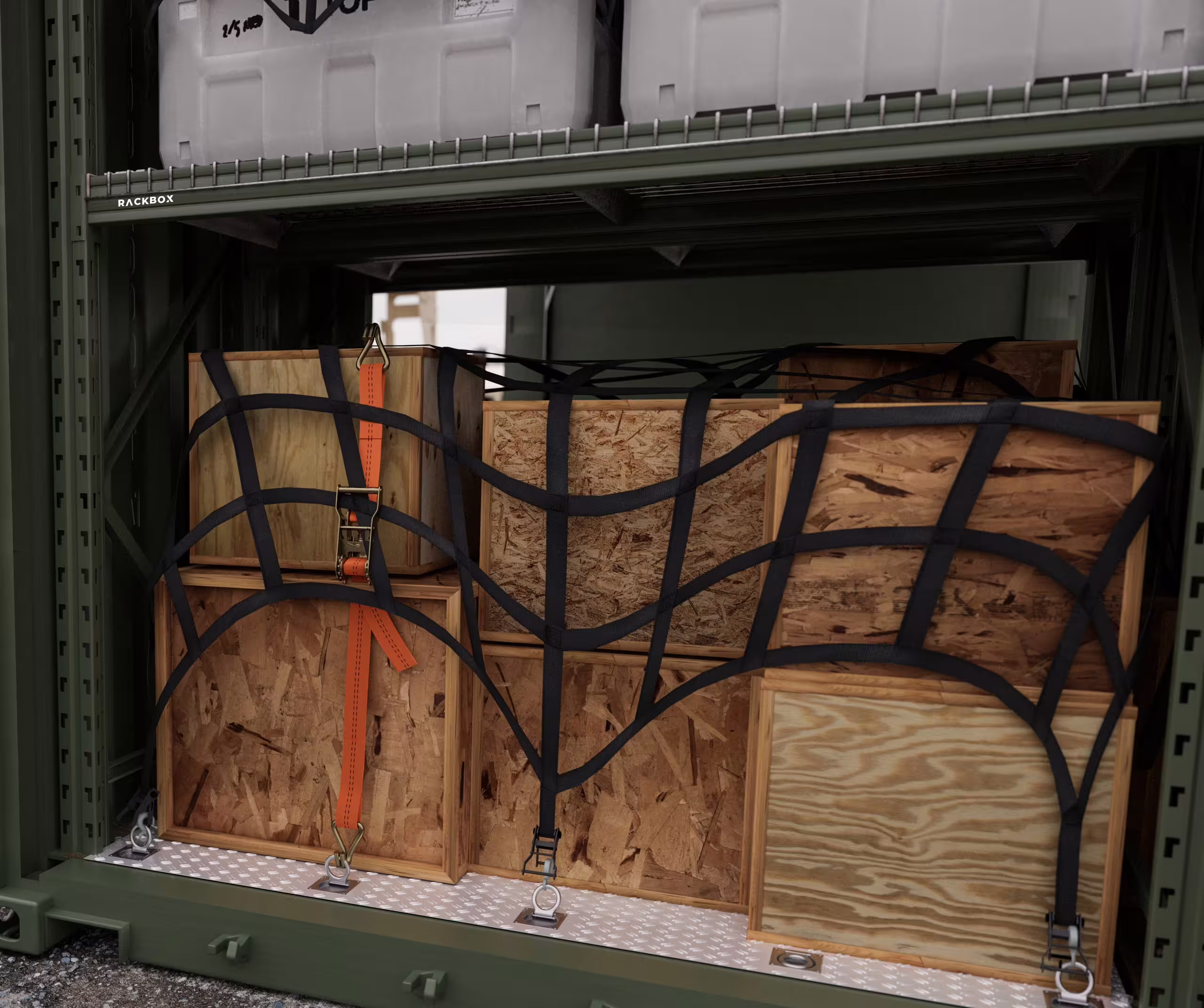 A fitted module bay loaded with plywood crates held by a cargo net and an orange ratchet strap, standing on a chequer-plate tray floor with tie-down rings, the structural upright stencilled RACKBOX and a mesh shelf of transit cases above