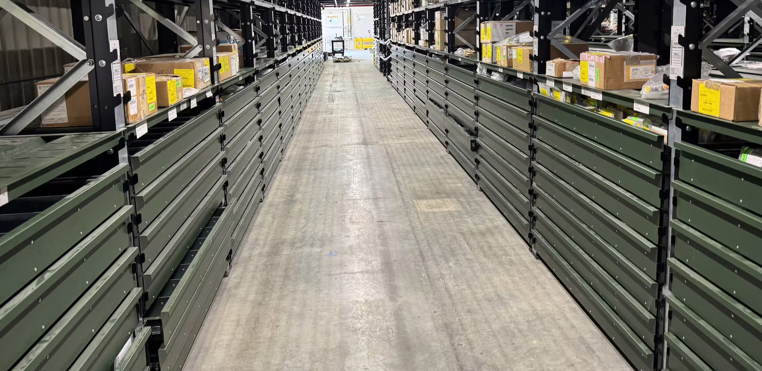 A long warehouse aisle running to a vanishing point, both sides filled from floor to waist height with rank after rank of closed green RackMezz drawer units