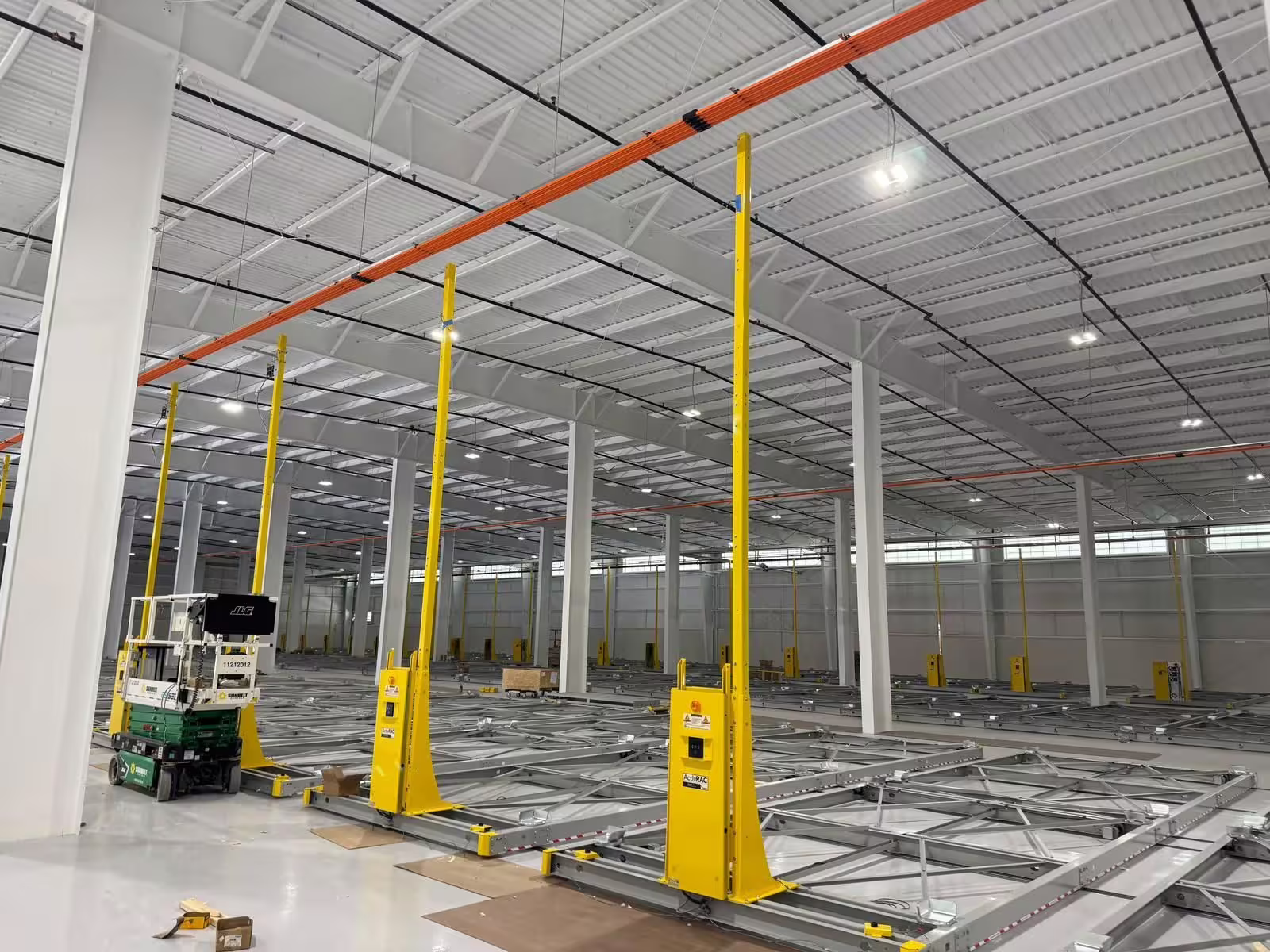 An empty steel-framed hall with RollingStack mobile-base rails set into the floor and yellow guide posts standing at the ends of each run