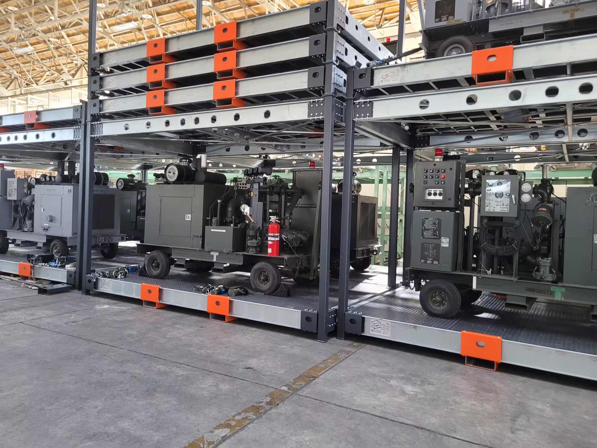 RollingStack crates stacked two high at close range, each level carrying generators and wheeled plant behind orange lashing markers
