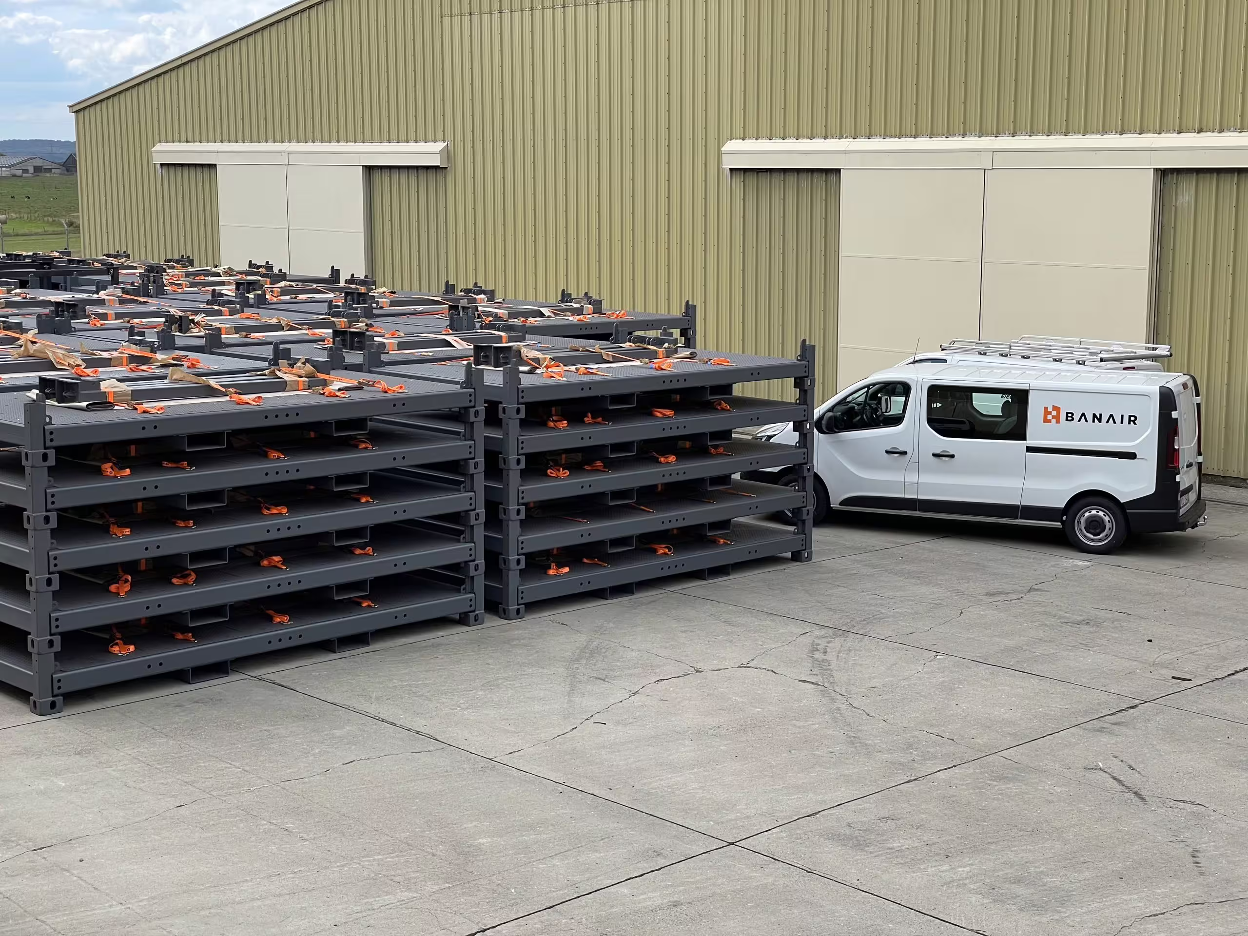 Two stacks of empty RollingStack frames standing in a yard, five and six levels high with their corner posts seated into each other and orange lashings across the decks